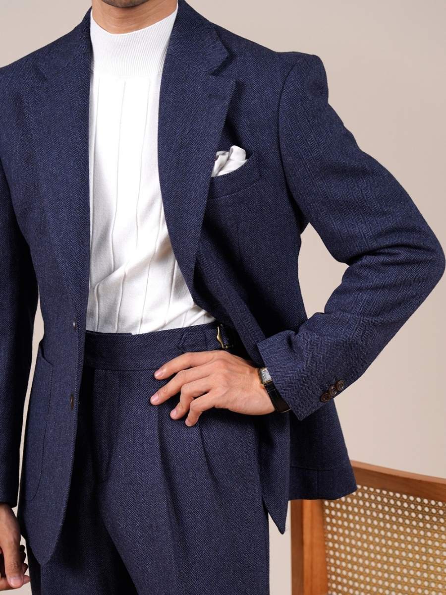 Man wearing navy blue herringbone suit with white knit sweater and pocket square