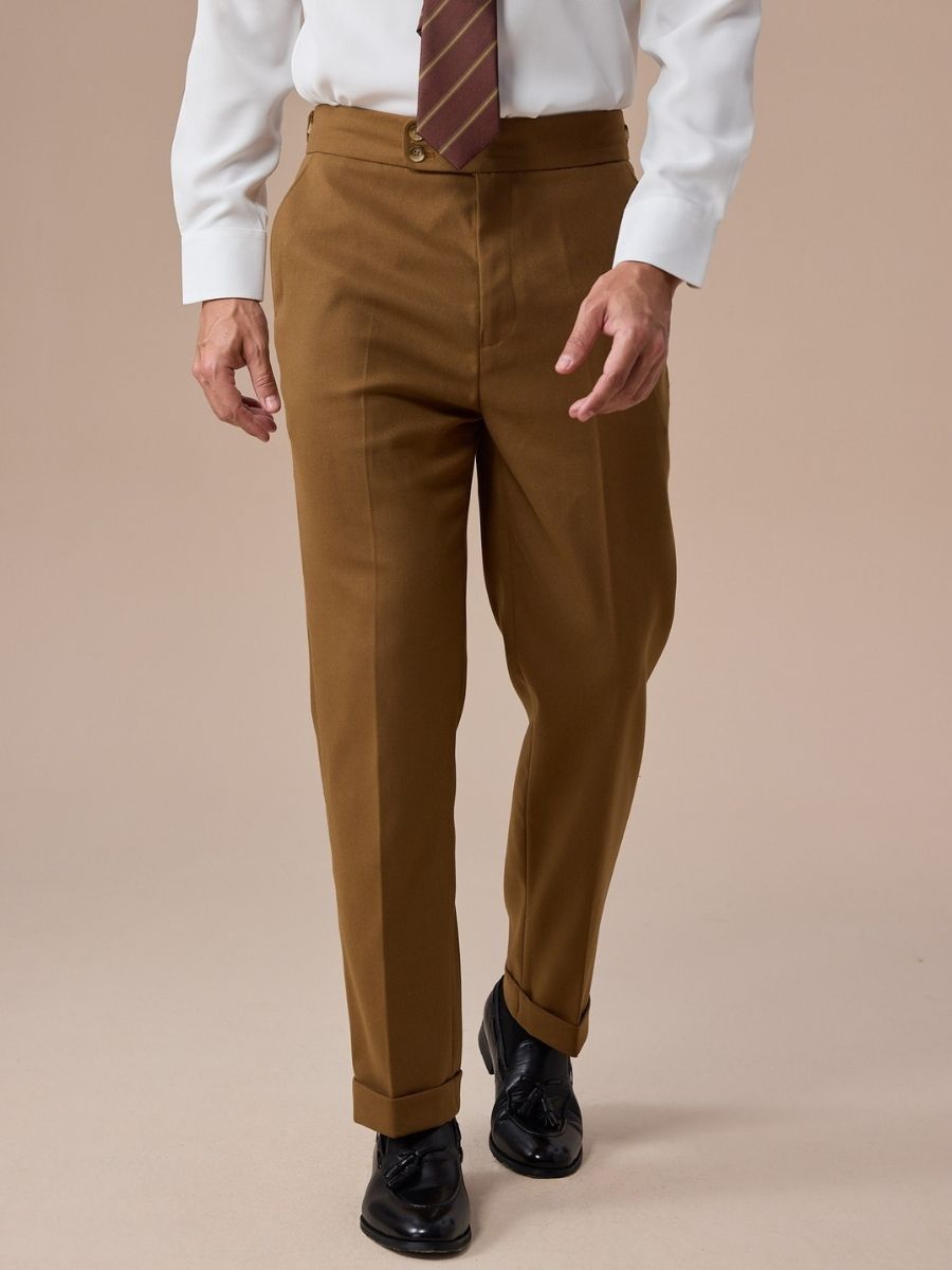 Man wearing brown tailored trousers with cuffs, white shirt, striped tie, and black leather tassel loafers