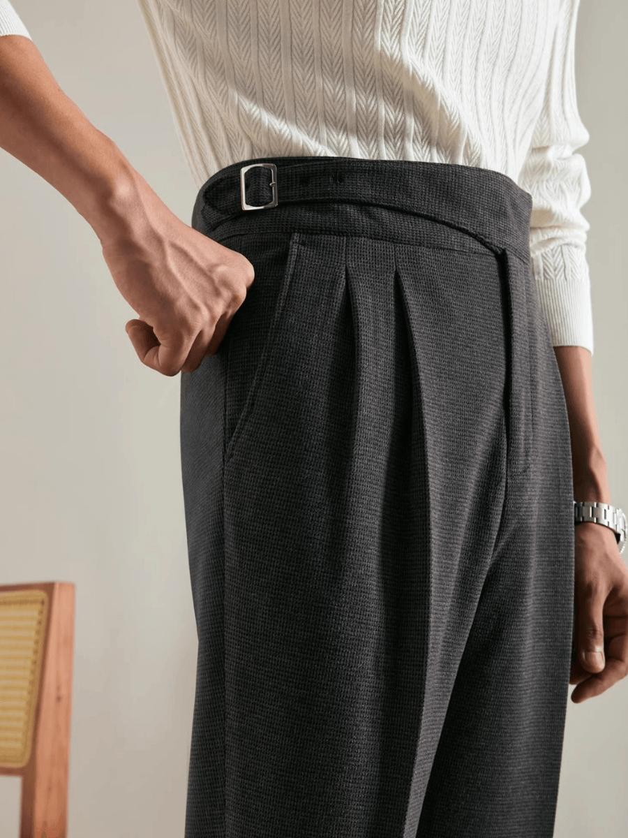 Close-up of waist wearing dark grey tailored trousers with side pockets and belt detail, paired with white knit sweater