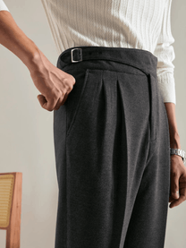 Close-up of waist wearing dark grey tailored trousers with side pockets and belt detail, paired with white knit sweater