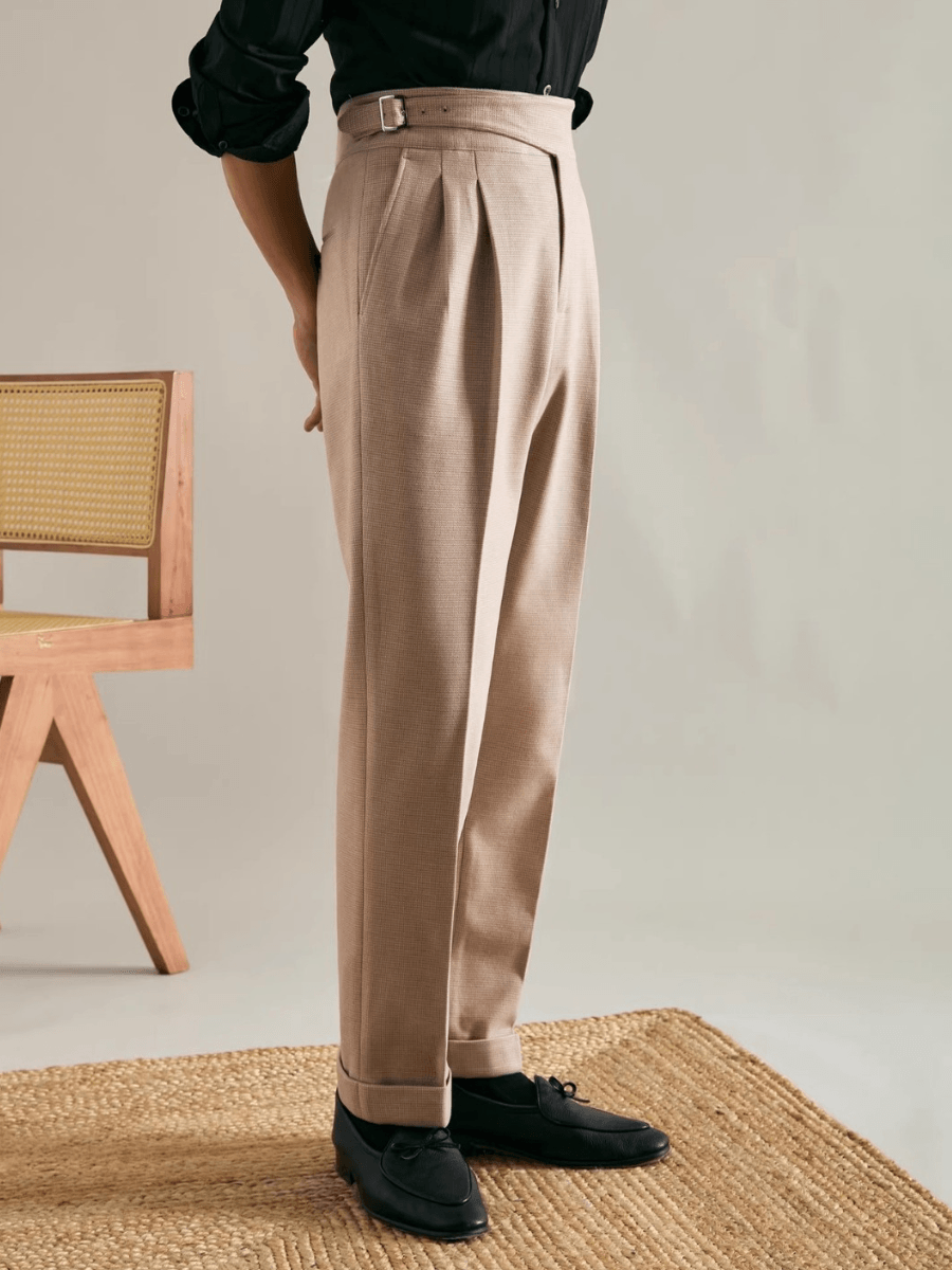 Side view of beige high-waisted pleated trousers paired with black loafers and rolled cuffs