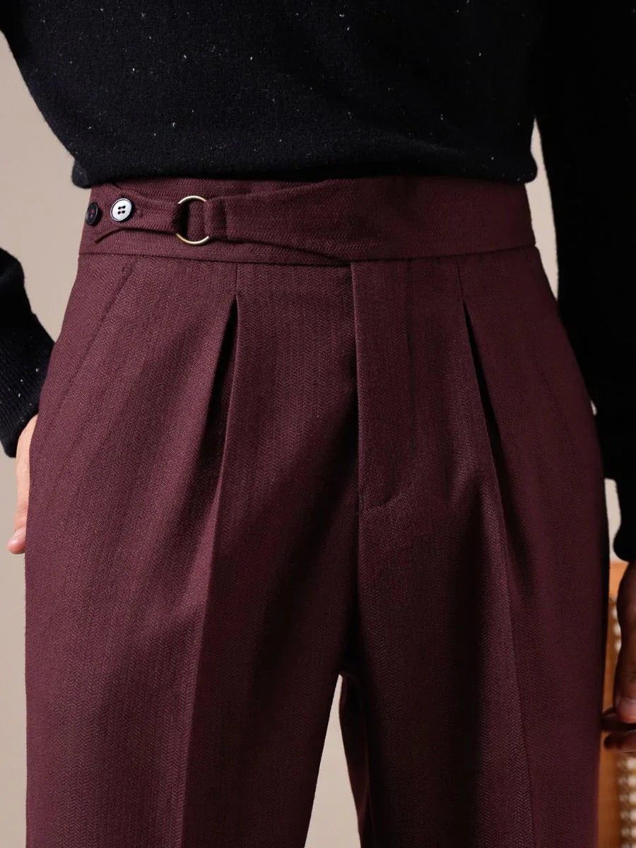 Close-up of men&#39;s high-waisted burgundy trousers with pleats and side button waistband detail