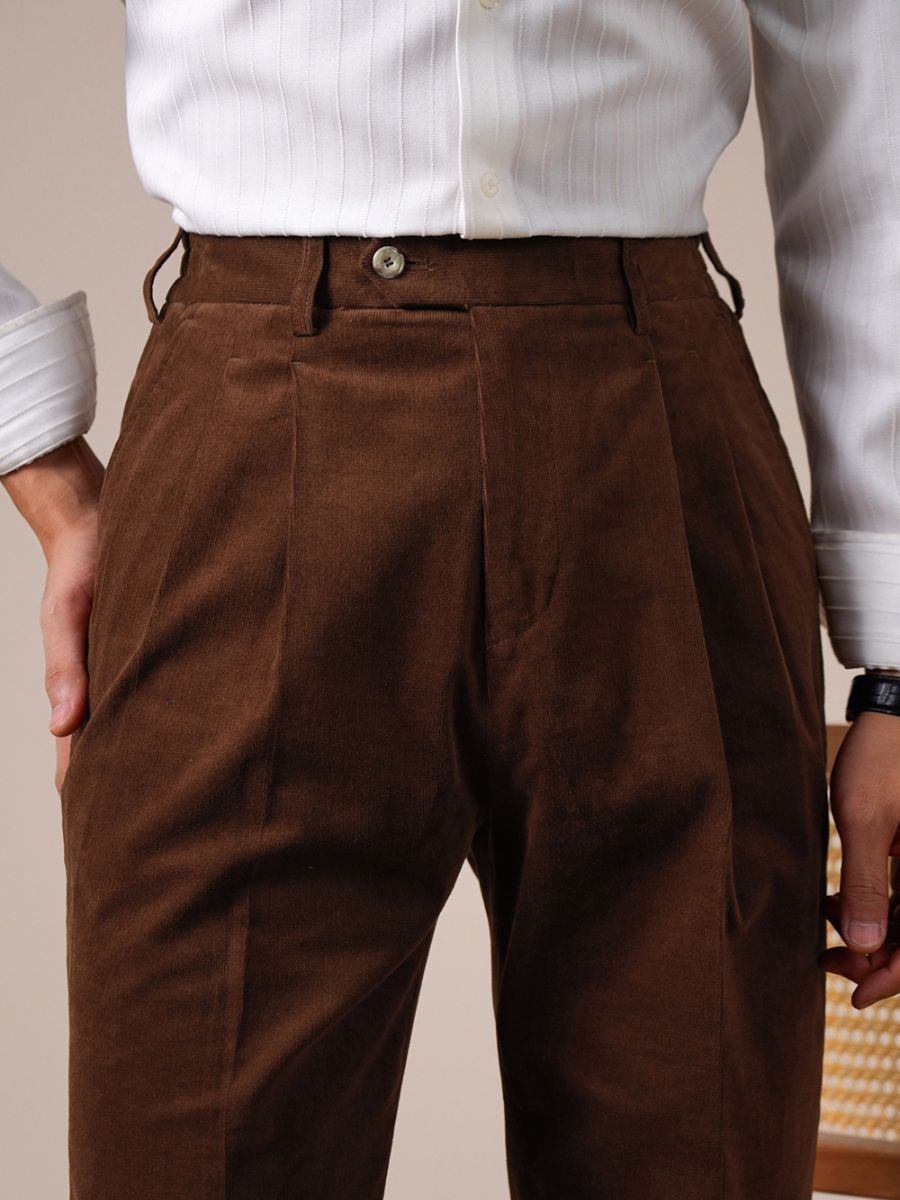 Close-up of brown corduroy pants with pleats worn with a white ribbed shirt