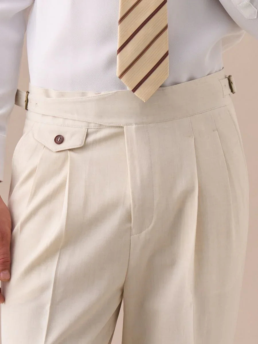 Close-up of beige high-waisted pleated trousers with buttoned side adjuster worn with white shirt and striped tie