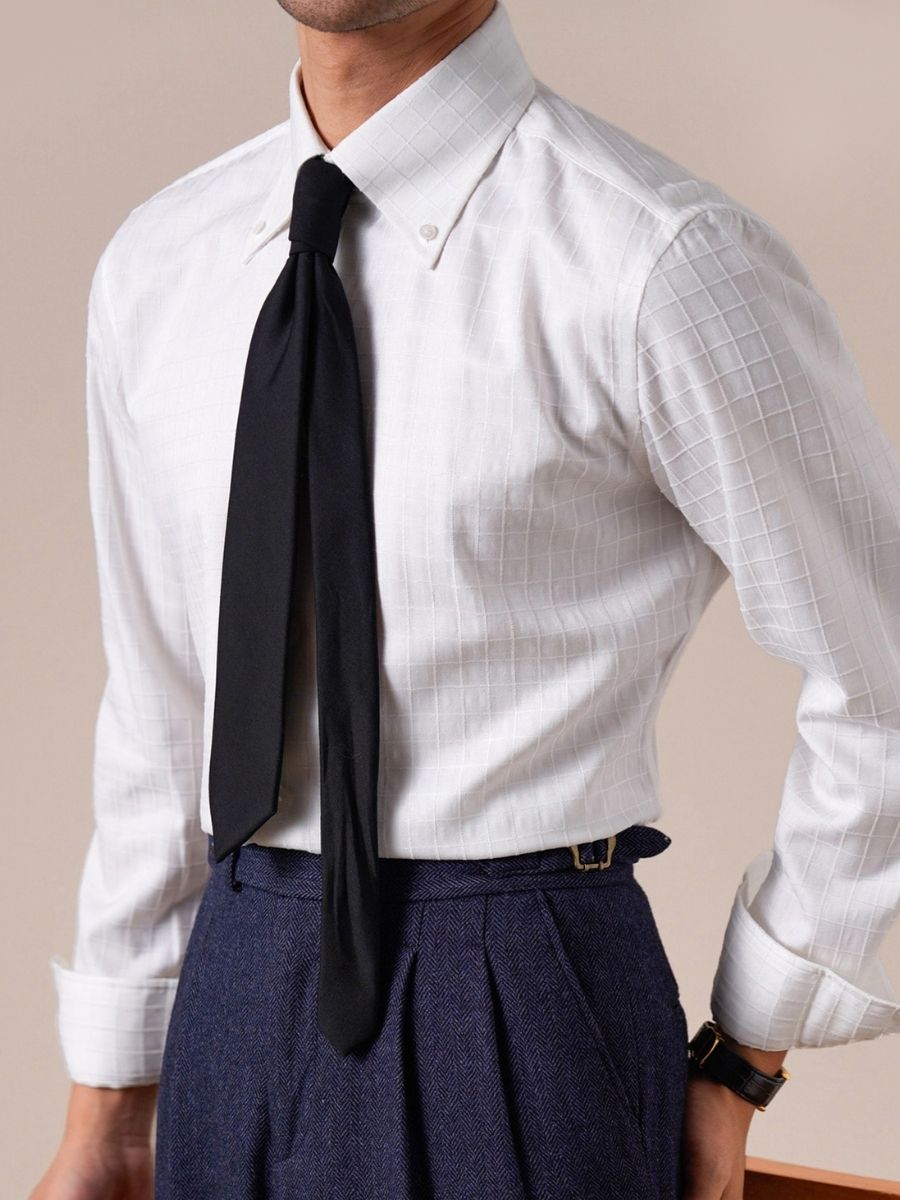 Man wearing white checkered dress shirt with button-down collar, black tie, and navy blue pleated trousers