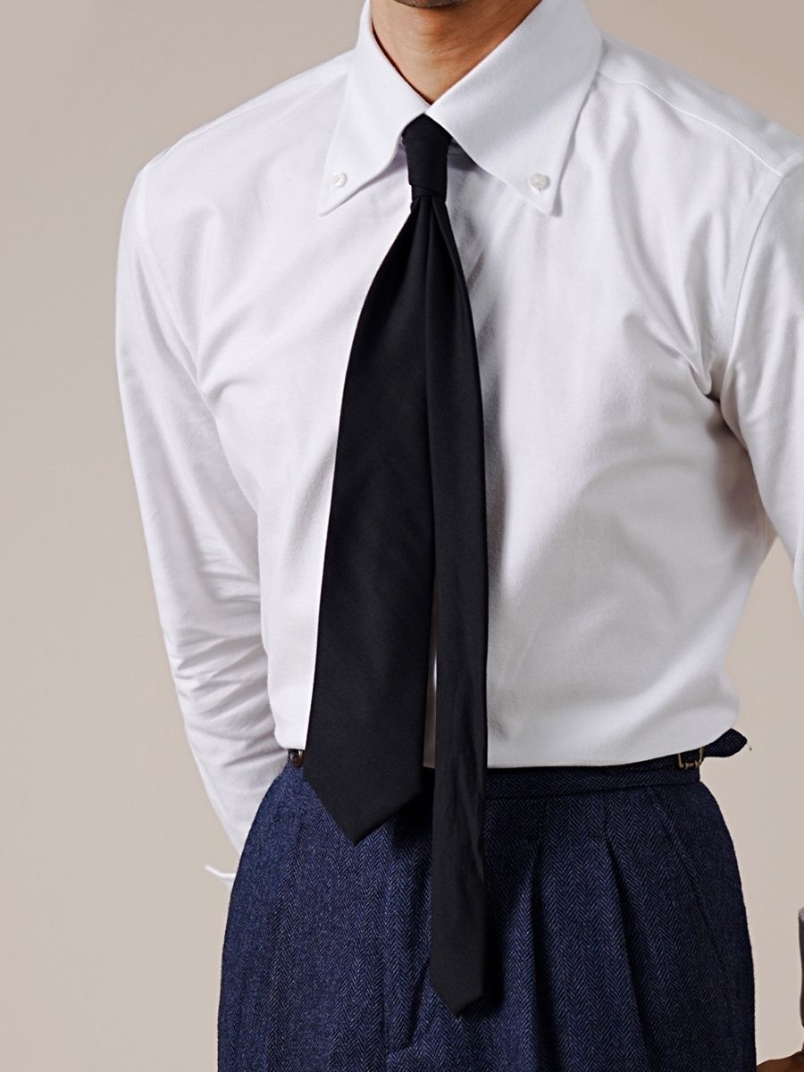 Man wearing a white button-down shirt, black necktie, and blue herringbone pleated trousers