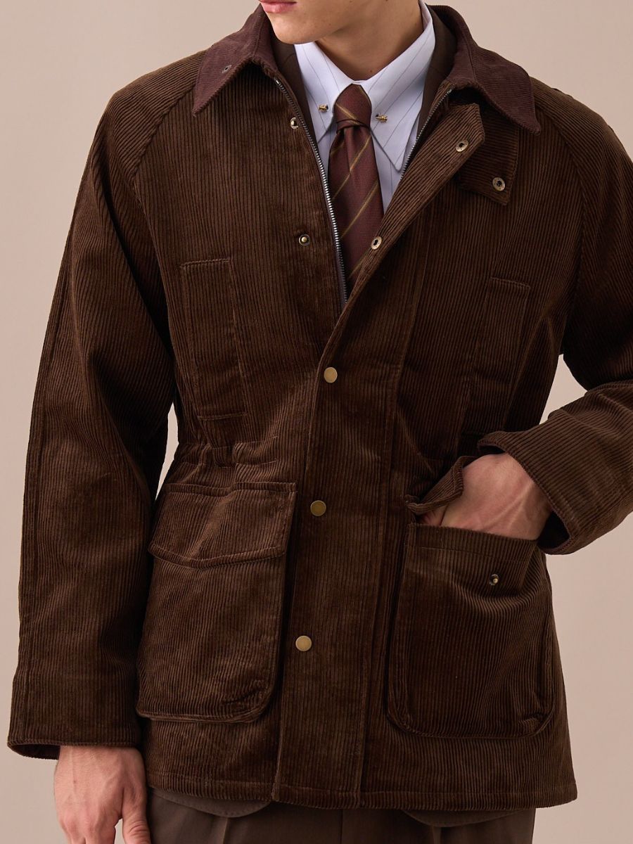 Man wearing brown corduroy jacket over white shirt and striped brown tie, hand in pocket