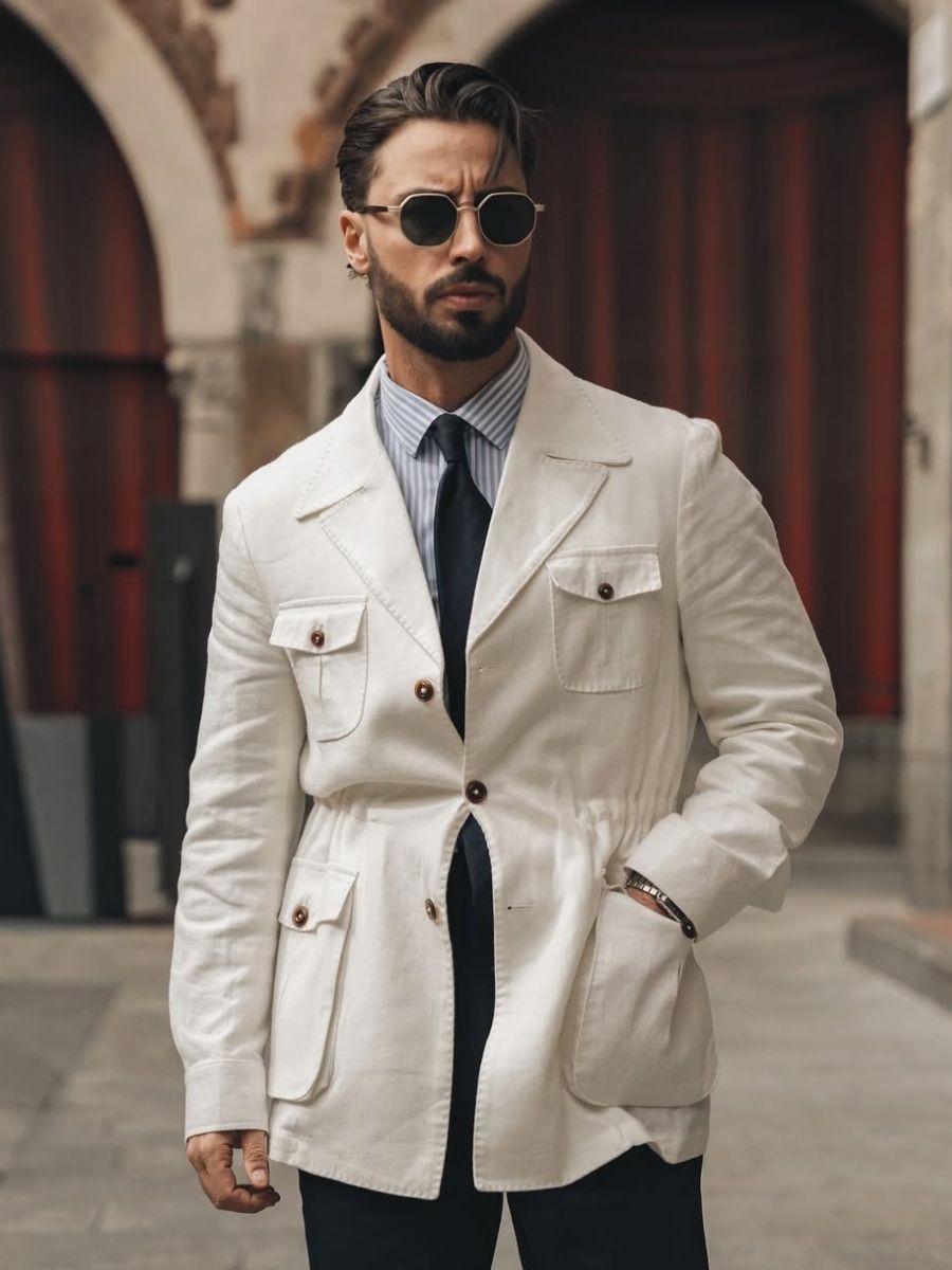 Stylish man wearing white linen jacket, striped shirt, black tie, and round sunglasses in urban archway